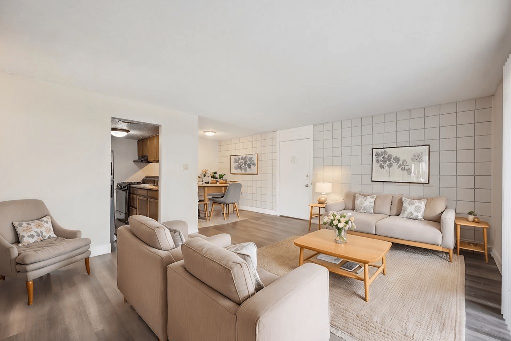 A living room with a grey couch, a brown couch, a grey armchair, a wooden coffee table, and a grey rug.