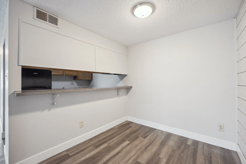 A kitchen area with a white wall and a wooden floor.