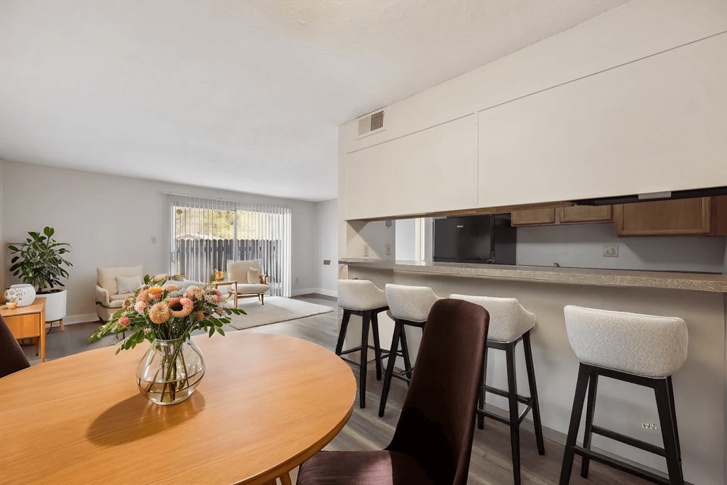 A kitchen with a table and chairs in the foreground and a dining area in the background.