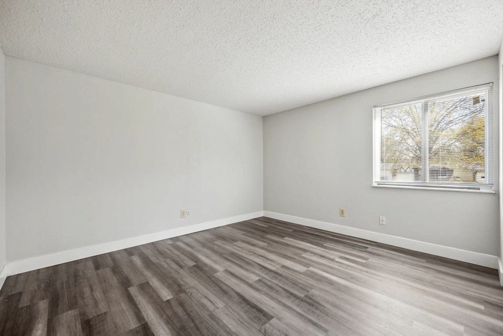 A room with wooden flooring and a window showing trees outside.