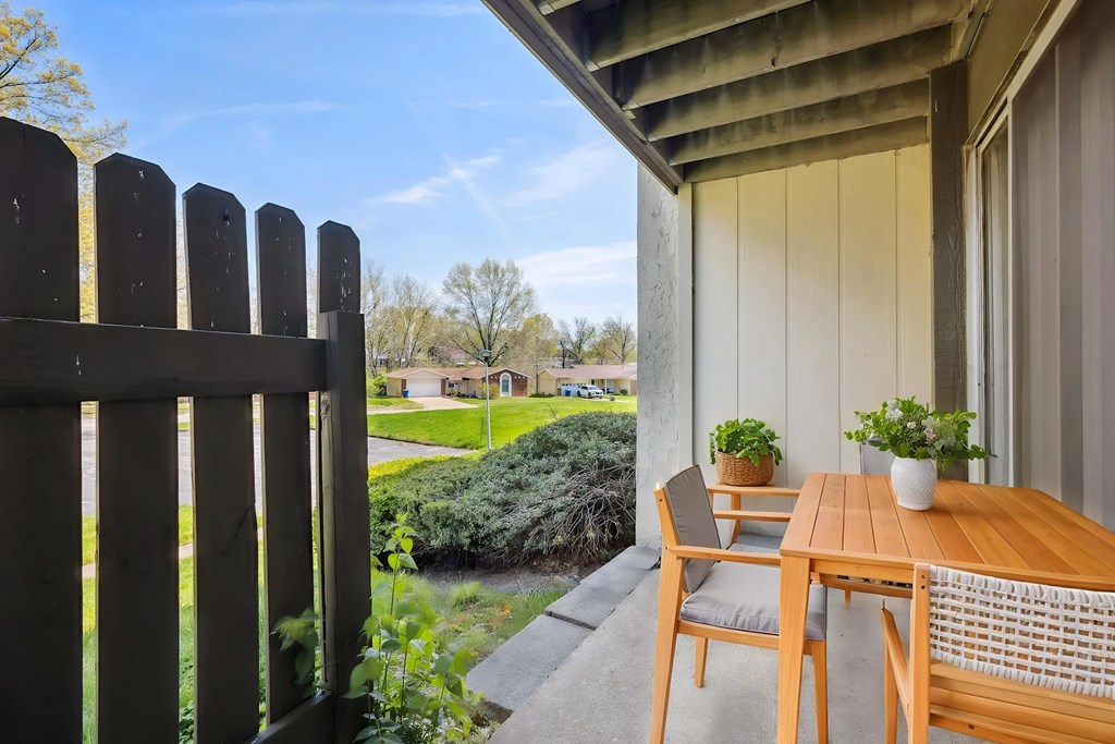 A wooden table and chairs are on a patio with a view of a backyard.