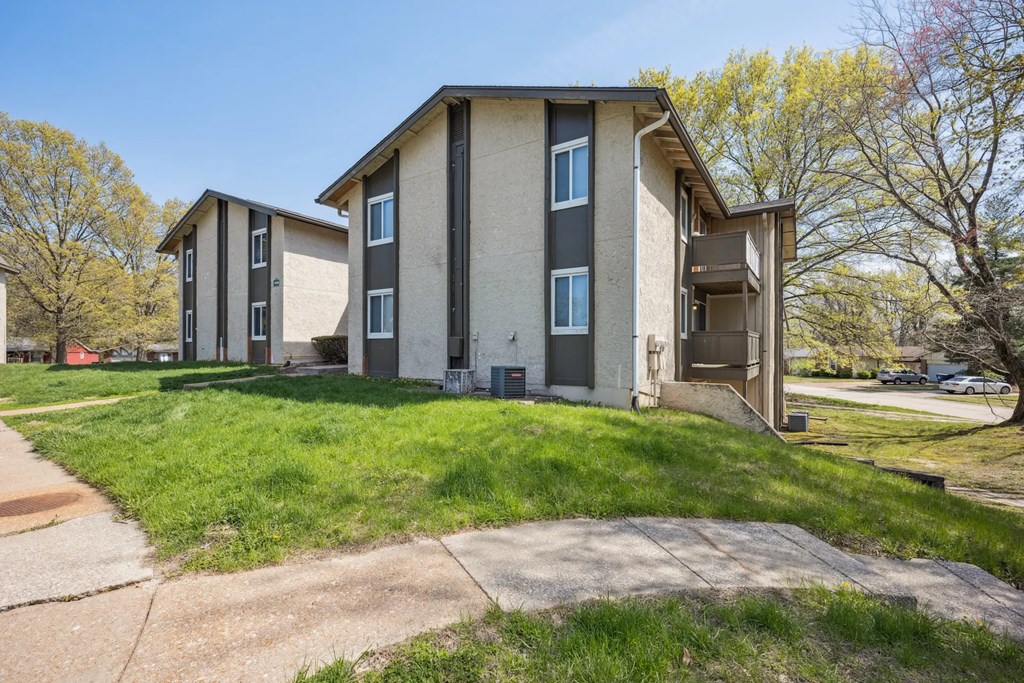 A building with a brown door and windows is surrounded by grass and trees.