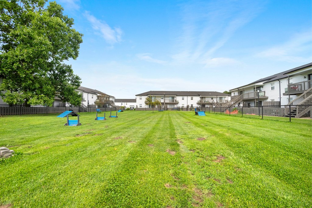 A grassy field with a fence and houses in the background.