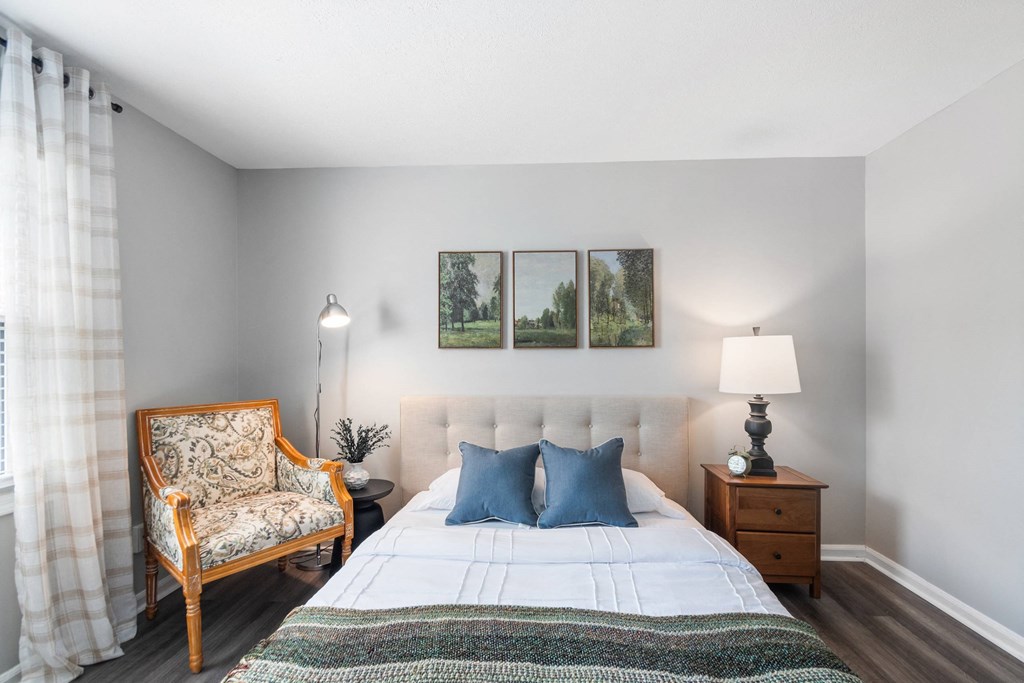 A bedroom with a bed, chair, and two pictures on the wall.
