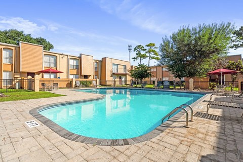 A swimming pool surrounded by a brick patio and apartment buildings.