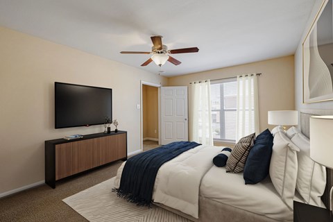 A bedroom with a bed, a television, and a ceiling fan.