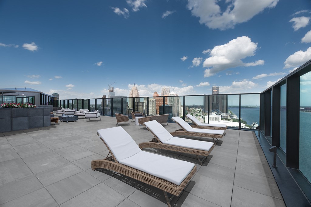 a rooftop lounge area with lounge chairs and a view of the city and the ocean
