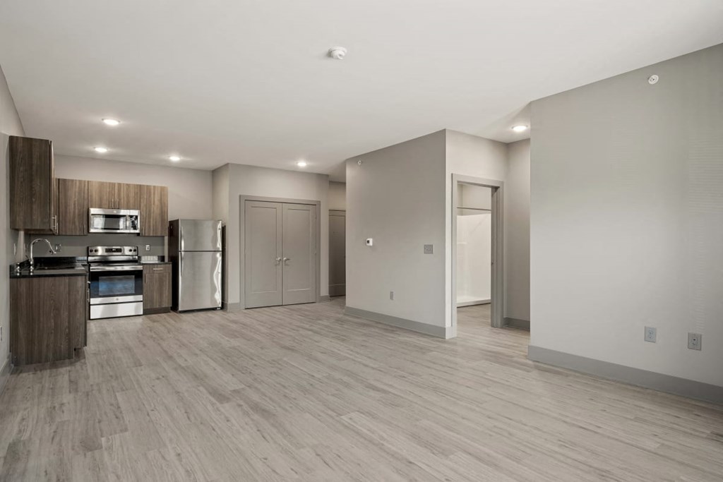 an empty living room with a kitchen with a stove and refrigerator