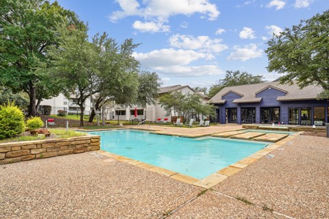 A swimming pool surrounded by a gravel area and trees.