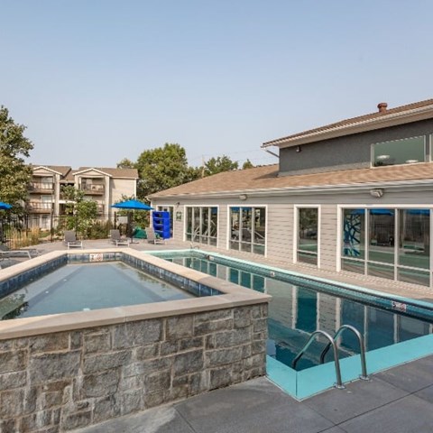 A swimming pool with a stone wall and a hot tub in the foreground.