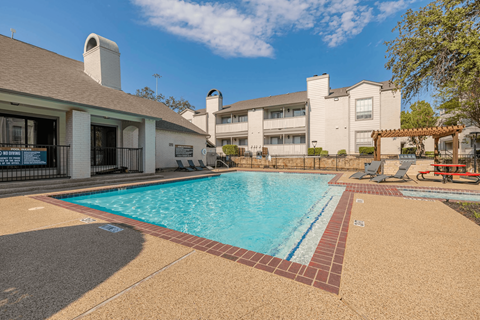 A swimming pool surrounded by a brick border and a building in the background.