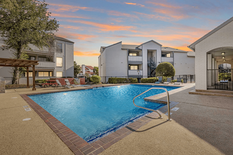 A swimming pool surrounded by a brick border with a sunset in the background.