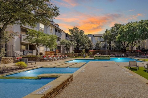 A swimming pool surrounded by apartment buildings at sunset.