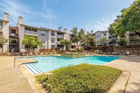 A swimming pool surrounded by bushes and trees in front of apartment buildings.