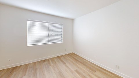 A room with wooden flooring and a window with blinds.