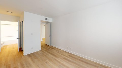A room with white walls and wooden flooring with a door open.