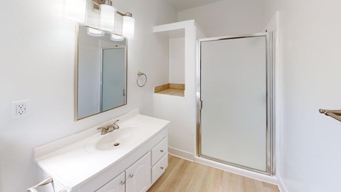 A white bathroom with a sink, mirror, and shower.