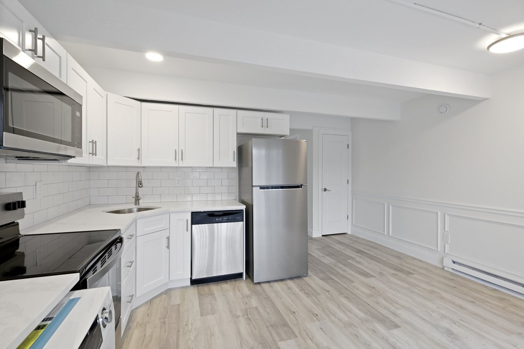 A modern kitchen with white cabinets and a wooden floor.