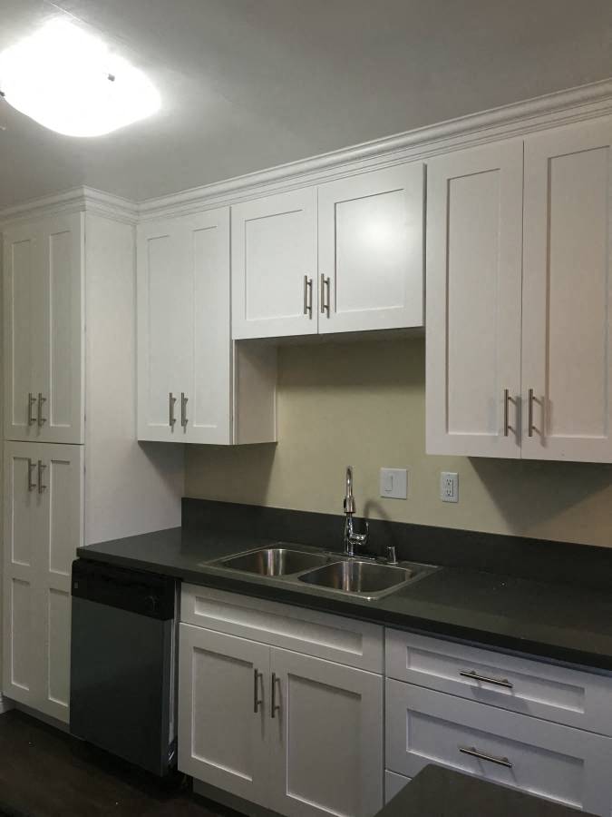 A kitchen with white cabinets and a black countertop.