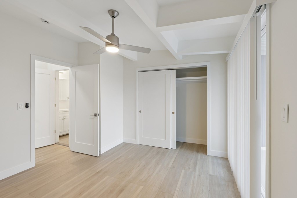 A room with a ceiling fan and light, wooden floors, and white walls with doors on either side.