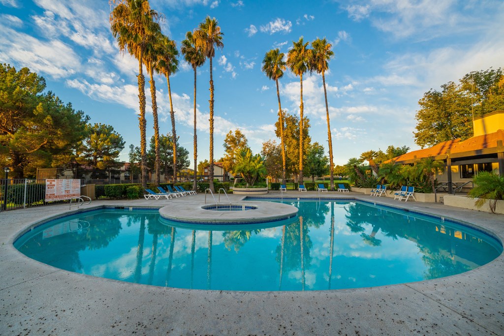 a swimming pool with a hot tub and chaise lounge chairs with palm trees in the background