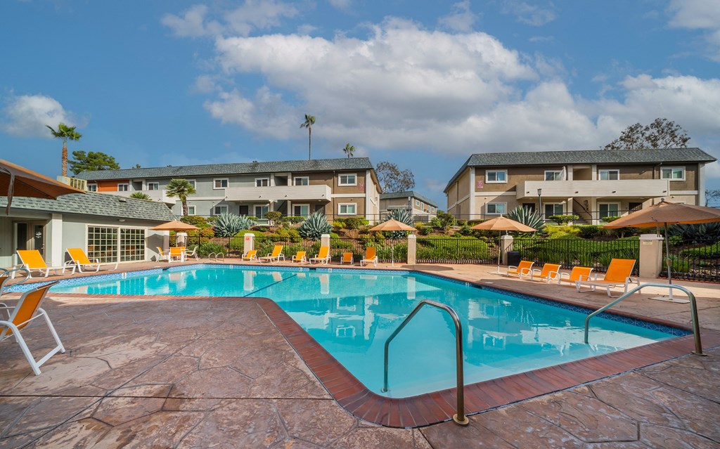 a swimming pool with orange chairs and buildings in the background