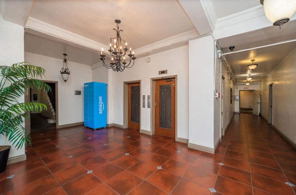 A blue recycling bin sits in the middle of a room with a chandelier hanging from the ceiling.