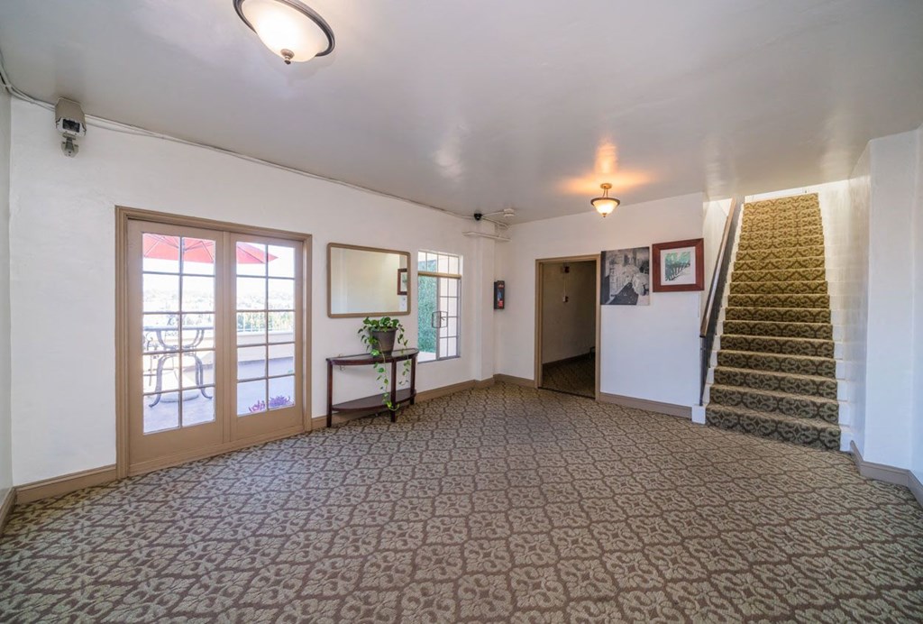 A room with a carpeted floor and a staircase on the right side.