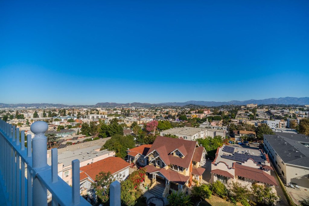 A white fence in front of a house with a view of a city and mountains in the background.