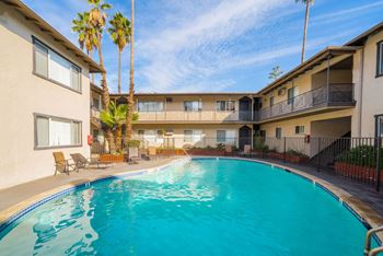 A swimming pool in front of a building with palm trees.