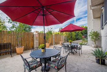 A patio with a table and chairs under a red umbrella.