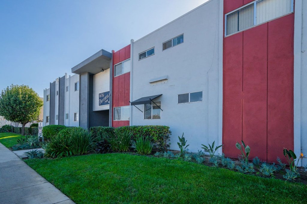 a white and red apartment building with a green yard in front of it