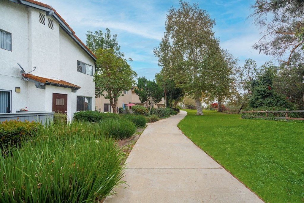 A white building with a red door is on the left side of a concrete walkway.