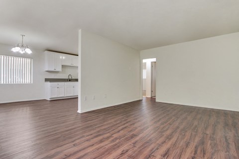 an empty living room and kitchen with wood flooring and white walls