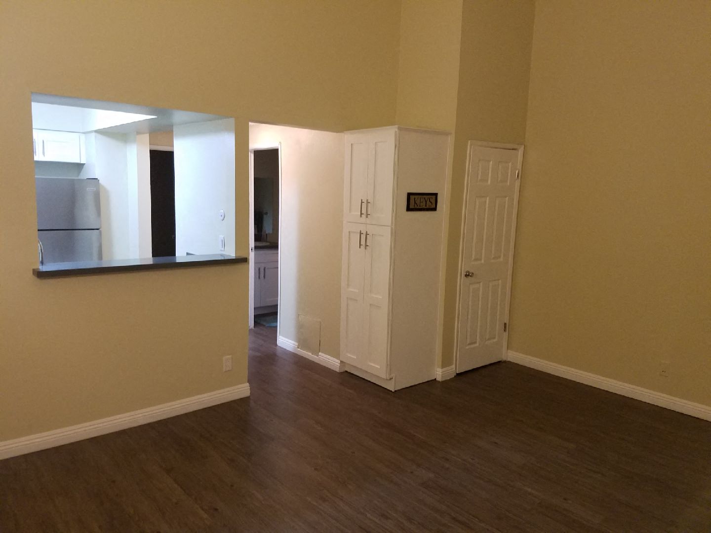 an empty living room with wooden floors and a door to the kitchen