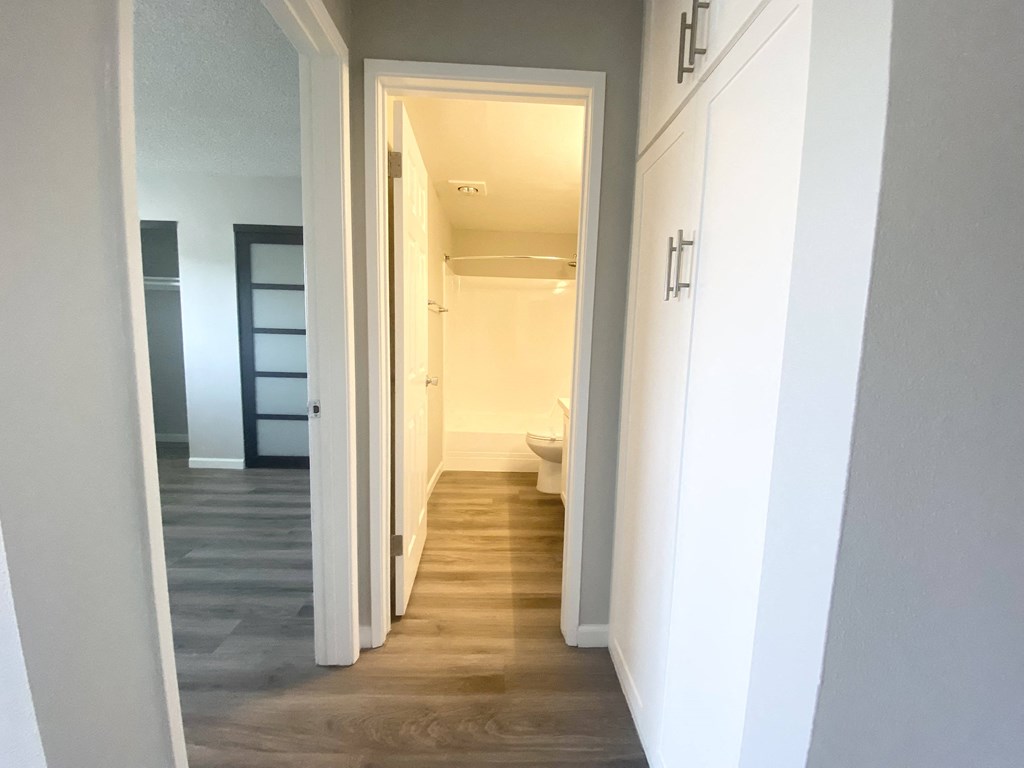 the hallway of a home with white cabinets and a bathroom