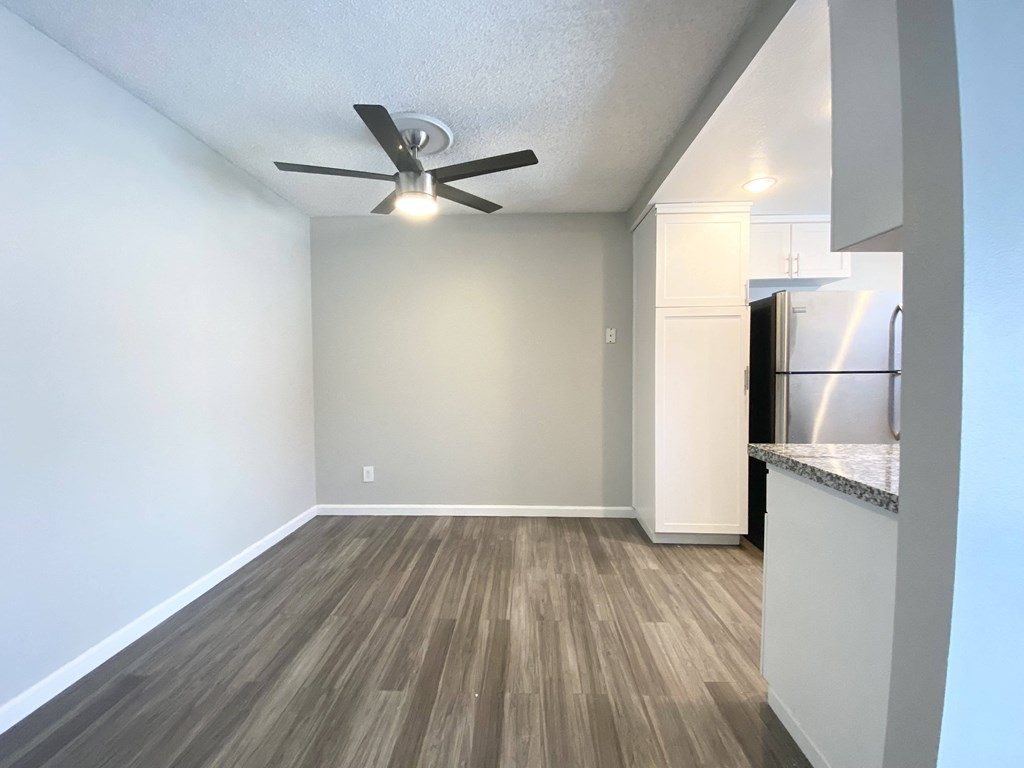 an empty living room with a ceiling fan and a kitchen