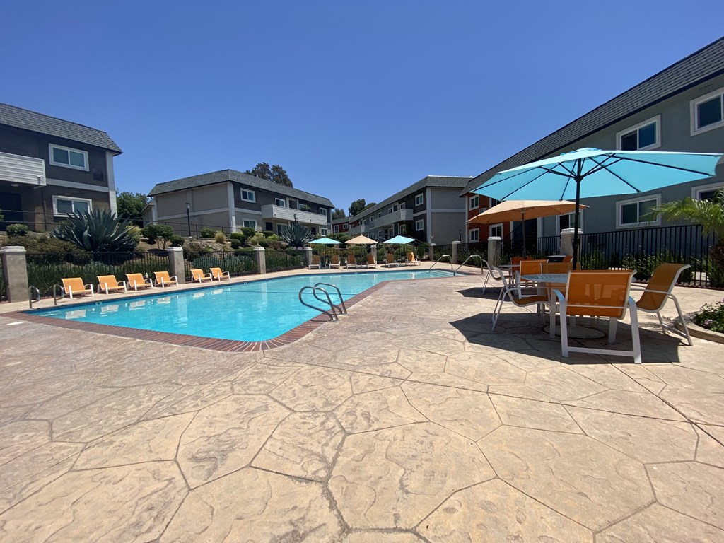 a swimming pool with chairs and umbrellas in front of apartment buildings