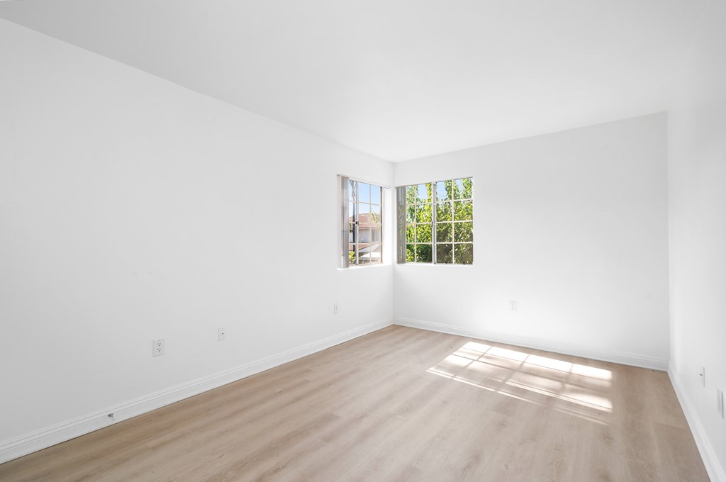 A large empty room with a window and wooden flooring.