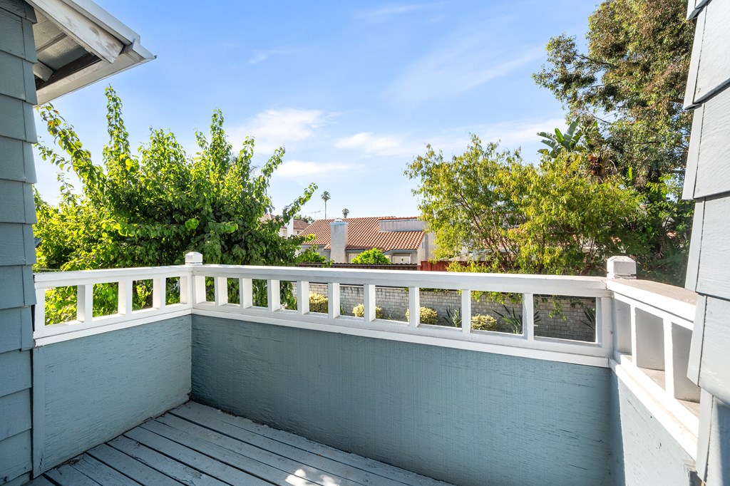 A balcony with a white railing and a view of a house and trees.