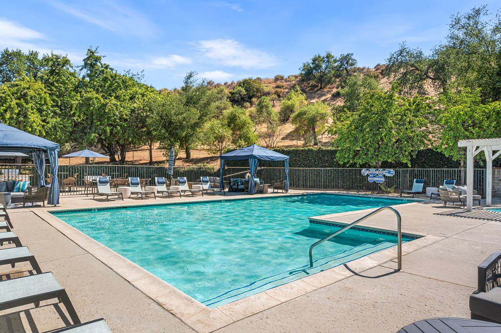 A large outdoor swimming pool surrounded by trees and lounge chairs.