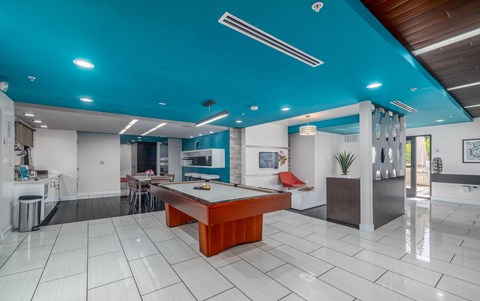 A room with a pool table and a kitchen area.