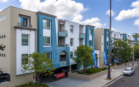 A row of modern apartment buildings with balconies and trees in front.