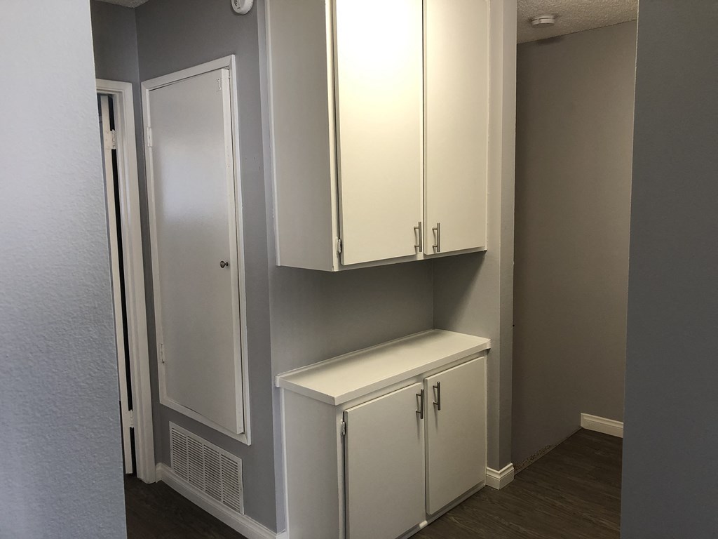 A white cabinet with a door is in the corner of a room.
