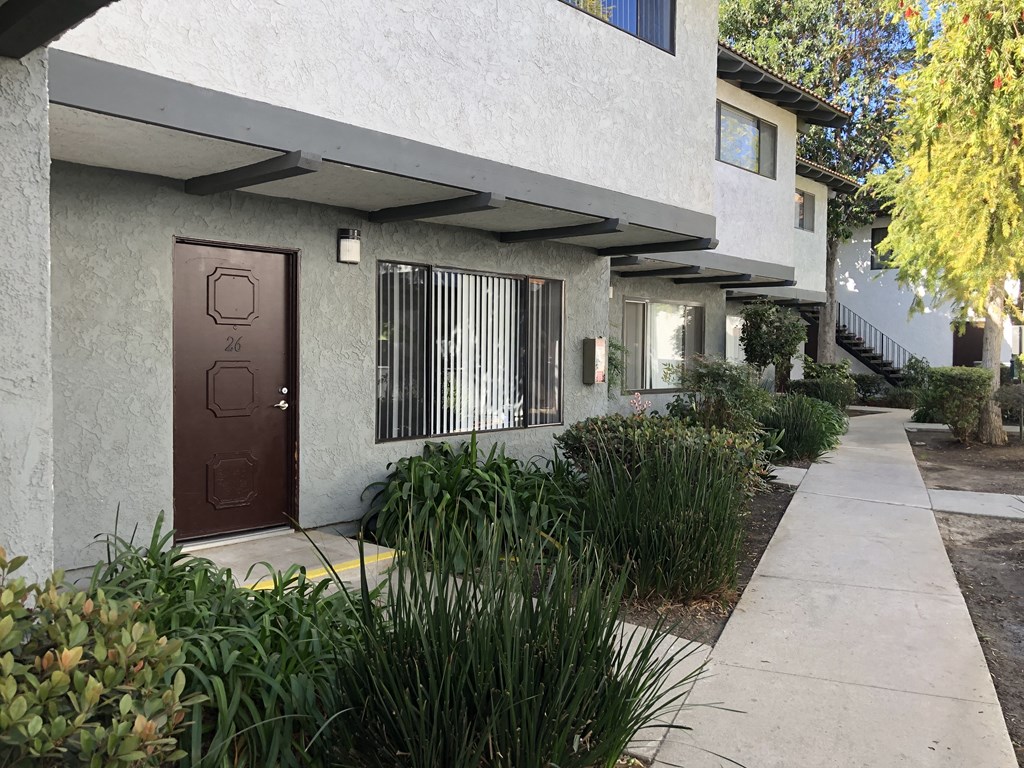 A brown door is on the left side of a white building.