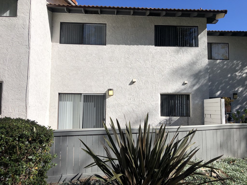 A white house with a grey fence and a green plant in front.