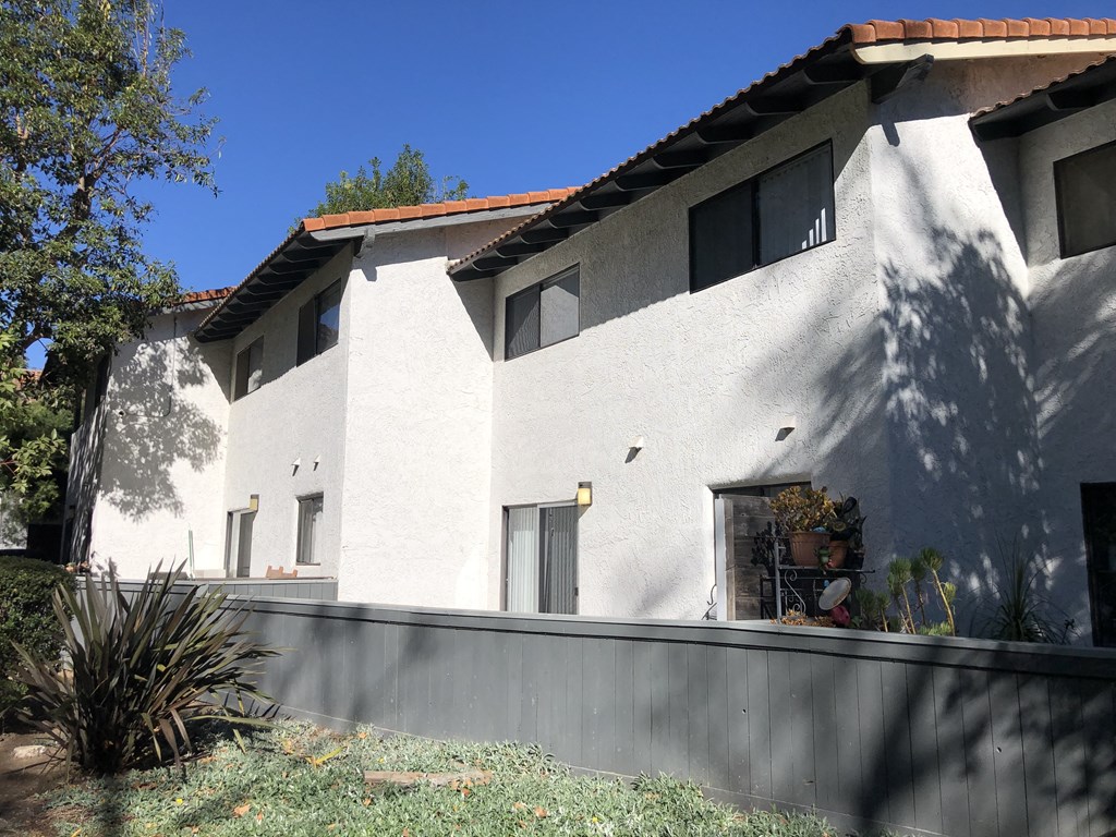 A white house with a red tile roof and a grey wall.