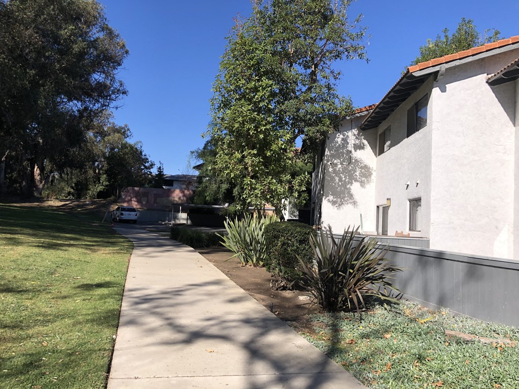 A white house with a brown roof and a tree in front of it.