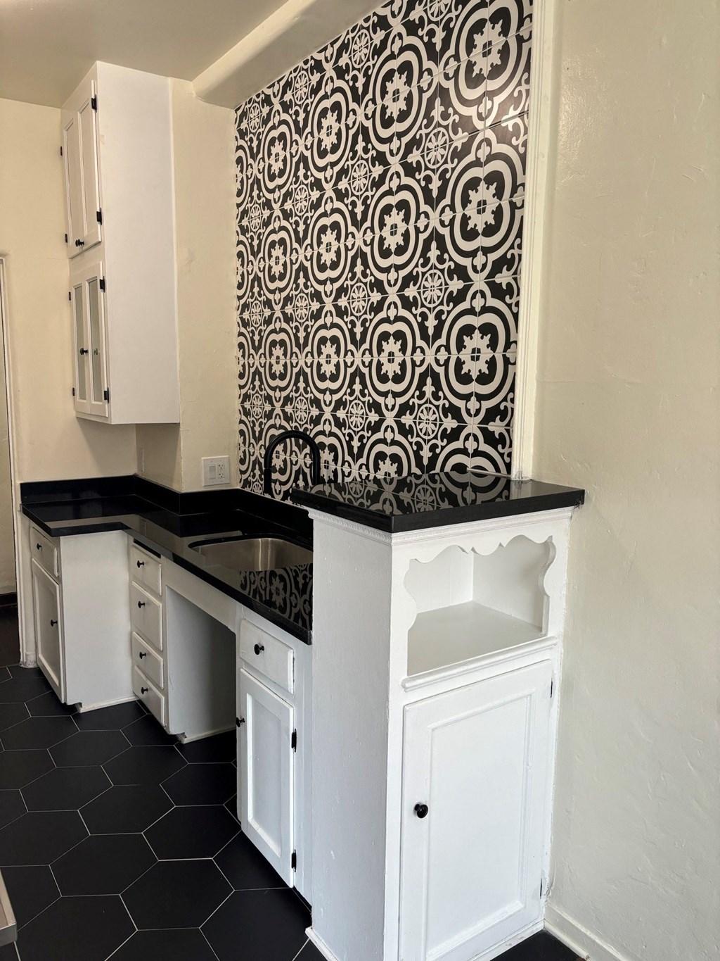 a kitchen with black counter tops and white cabinets and a black and white wallpaper