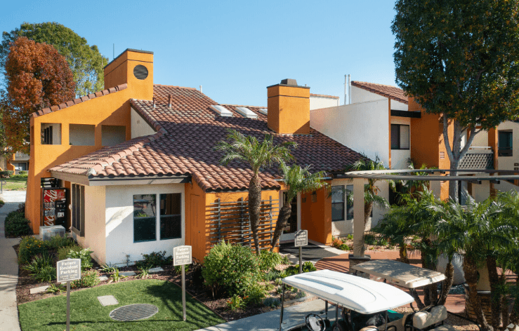 A yellow house with a red tile roof and a white surfboard leaning against it.